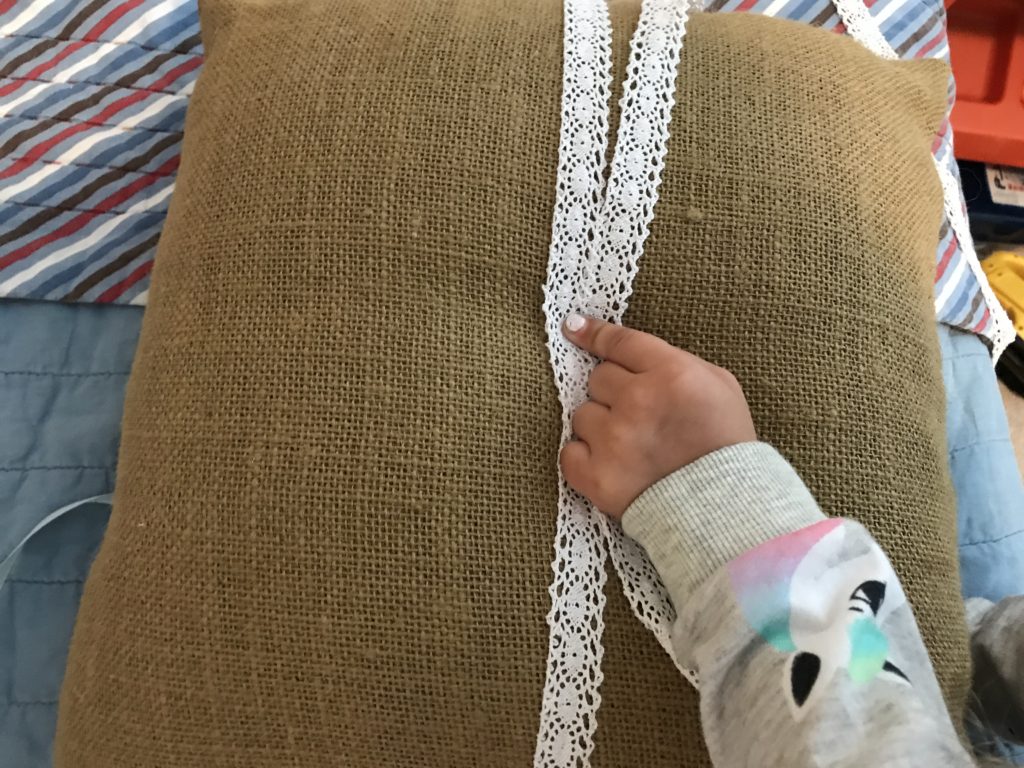 Tying on the white-lacey ribbon to upgrade our burlap porch pillow for Christmas.