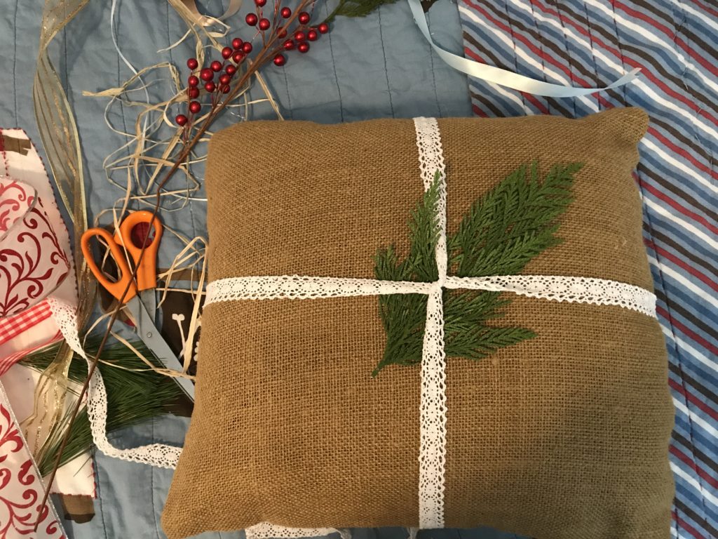 Adding evergreen to burlap pillow. Step 2 in upgrading front porch pillow into a burlap front porch rocking chair Christmas pillow.